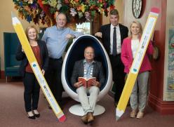 2 Men and 2 Women Standing holding pencils and one man sitting in egg chair reading